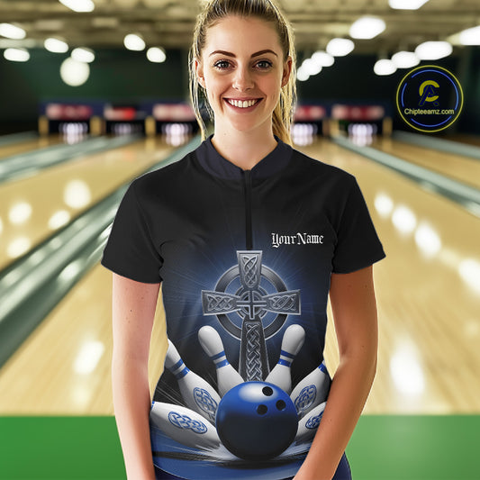 Female model front view in bowling lane wearing black quarter zip shirt with blue Celtic cross design and explosive bowling pin action graphic