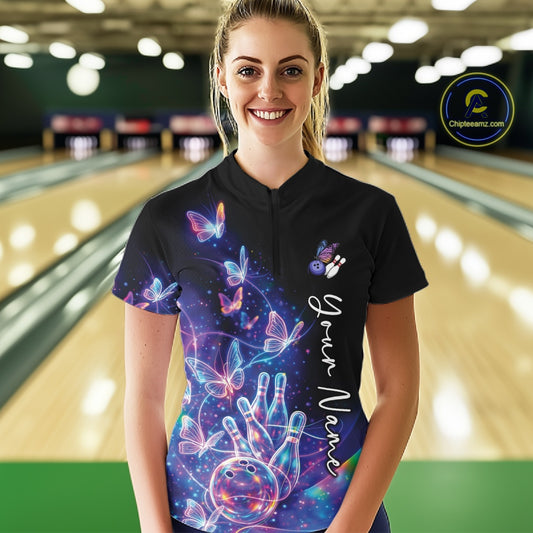 Female model wearing a black bowling quarter zip with starry galaxy artwork, neon swirls, and hologram butterflies, front view inside a bowling alley