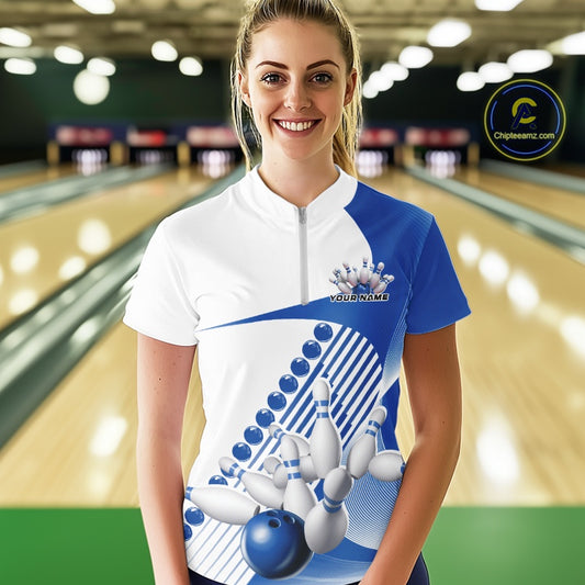 Front view of a female model in a white and blue bowling quarter zip featuring sweeping geometric stripes and dynamic bowling strike graphics at the bowling lane.