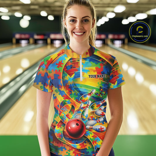Female model in a bowling lane wearing a colorful quarter-zip shirt, autism puzzle bowling ball and pins artwork with vibrant graphic style.