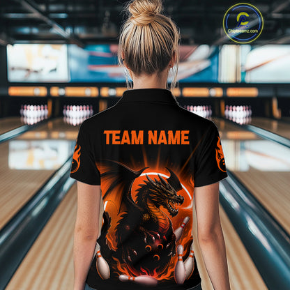 A woman viewed from behind wearing a black short-sleeve bowling shirt with a large fiery dragon graphic and orange 'TEAM NAME' text on the back, standing in a bowling alley.