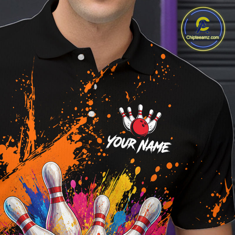 A close-up of a person wearing a black short-sleeve polo shirt with a colorful bowling-themed graphic print. The design features orange paint splatters, white bowling pins, a red bowling ball, and the customizable text 'YOUR NAME'.