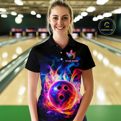 A woman stands in a bowling alley wearing a black short-sleeve polo shirt with a vibrant, colorful graphic of a glowing bowling ball surrounded by flames. The shirt features a custom name placeholder and a circular logo on the left chest.