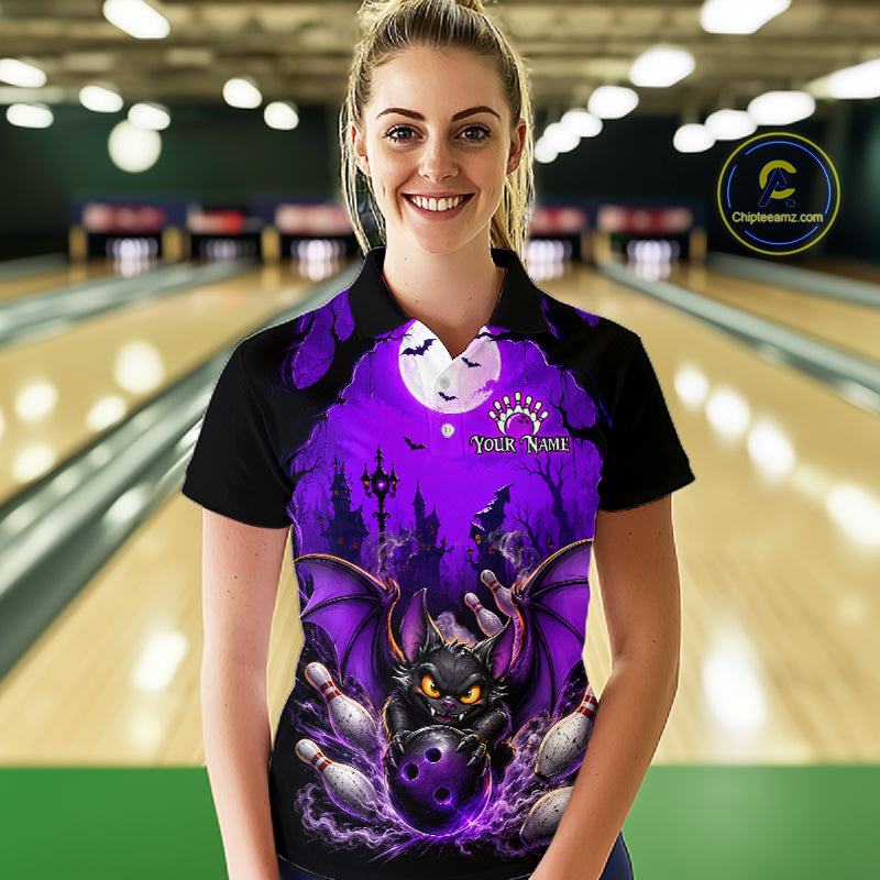 A woman wearing a black polo shirt with a vibrant purple and black Halloween-themed bat graphic, standing in a bowling alley. The shirt features a purple full moon, a black bat with glowing eyes, bowling pins, and the text 'YOUR NAME' 