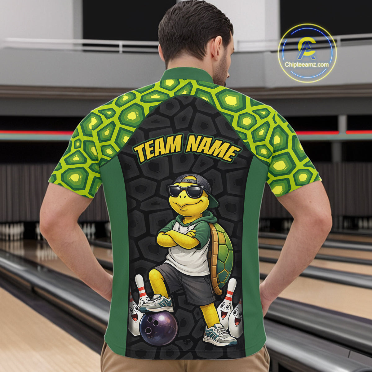 A man viewed from behind wearing a custom bowling shirt with a green and yellow turtle pattern on the sleeves and shoulders, a dark gray textured back panel, and a cartoon turtle graphic with the text 'TEAM NAME'. The background shows bowling lanes.