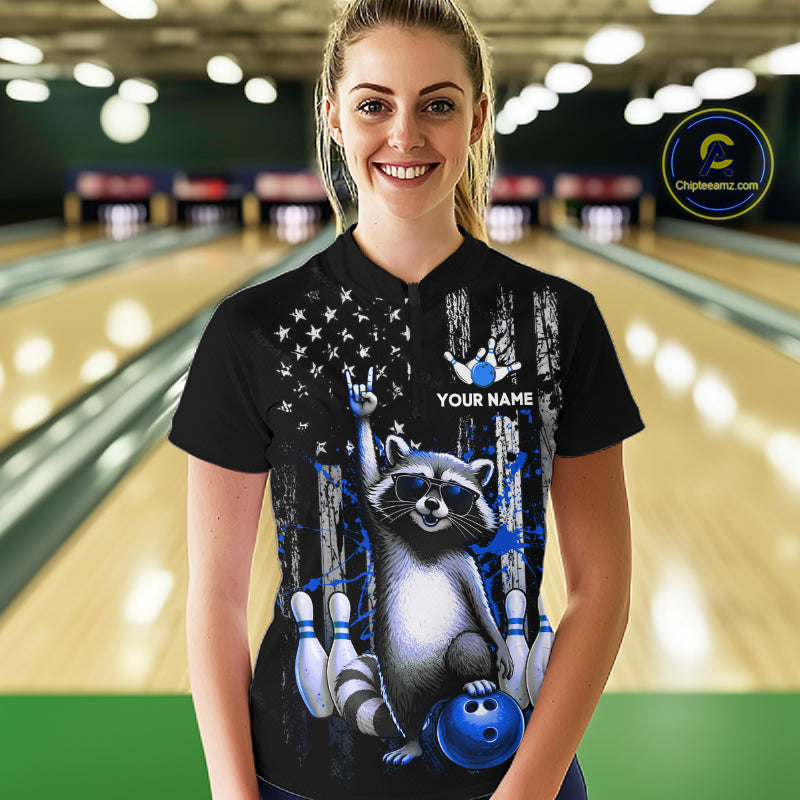 Person wearing a black shirt with a raccoon graphic and text in a bowling alley.