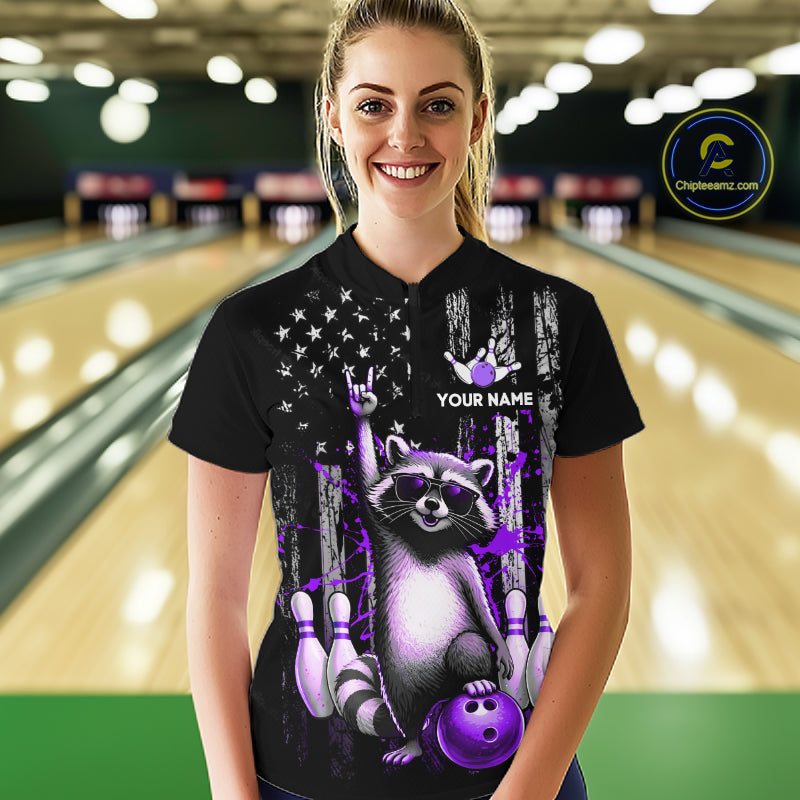 Person wearing a black shirt with a raccoon graphic and text in a bowling alley.