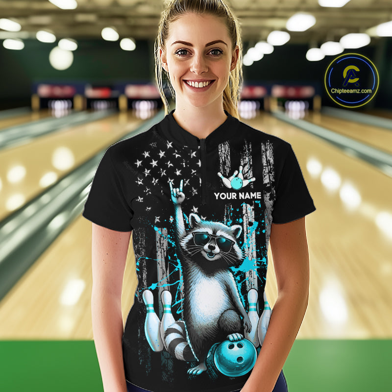 Person wearing a black shirt with a raccoon graphic and text in a bowling alley.