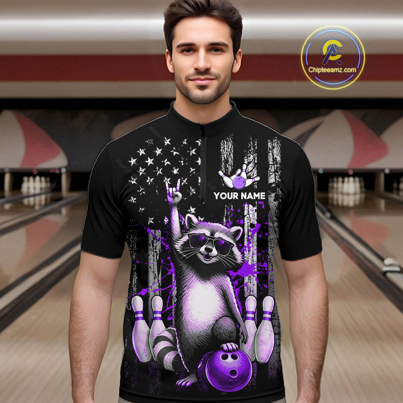 Man wearing a black bowling shirt with a raccoon design in a bowling alley.