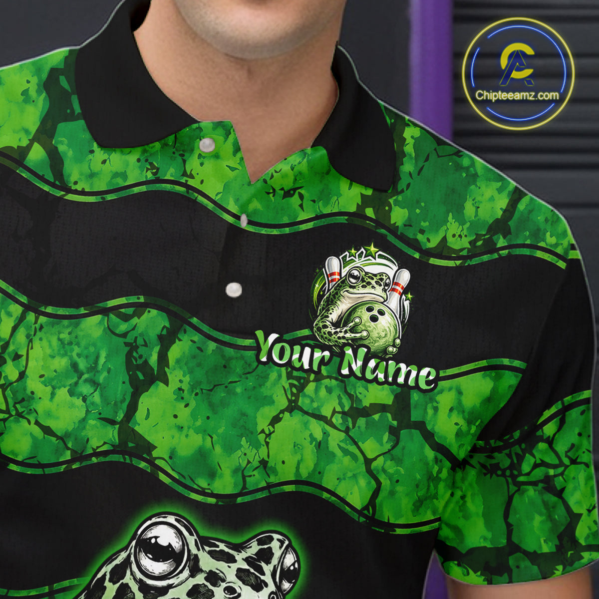 A close-up of a custom green and black frog-themed polo shirt worn by a model. The shirt features a green and black mottled pattern, a black collar, and custom graphic prints including a frog mascot, the text 'Your Name', and a large frog head at the bottom.