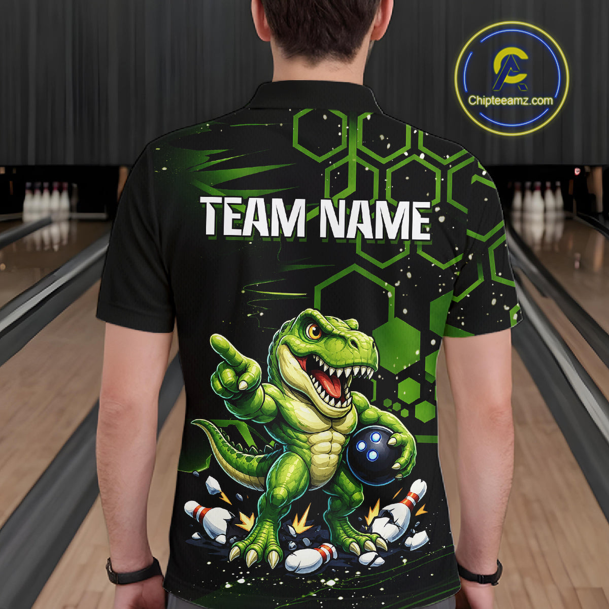 A person standing in a bowling alley viewed from behind, wearing a black short-sleeve bowling shirt with a large green dinosaur graphic, bowling pins, hexagon pattern, and the text 'TEAM NAME' on the back. A circular 'Chipteeamz.