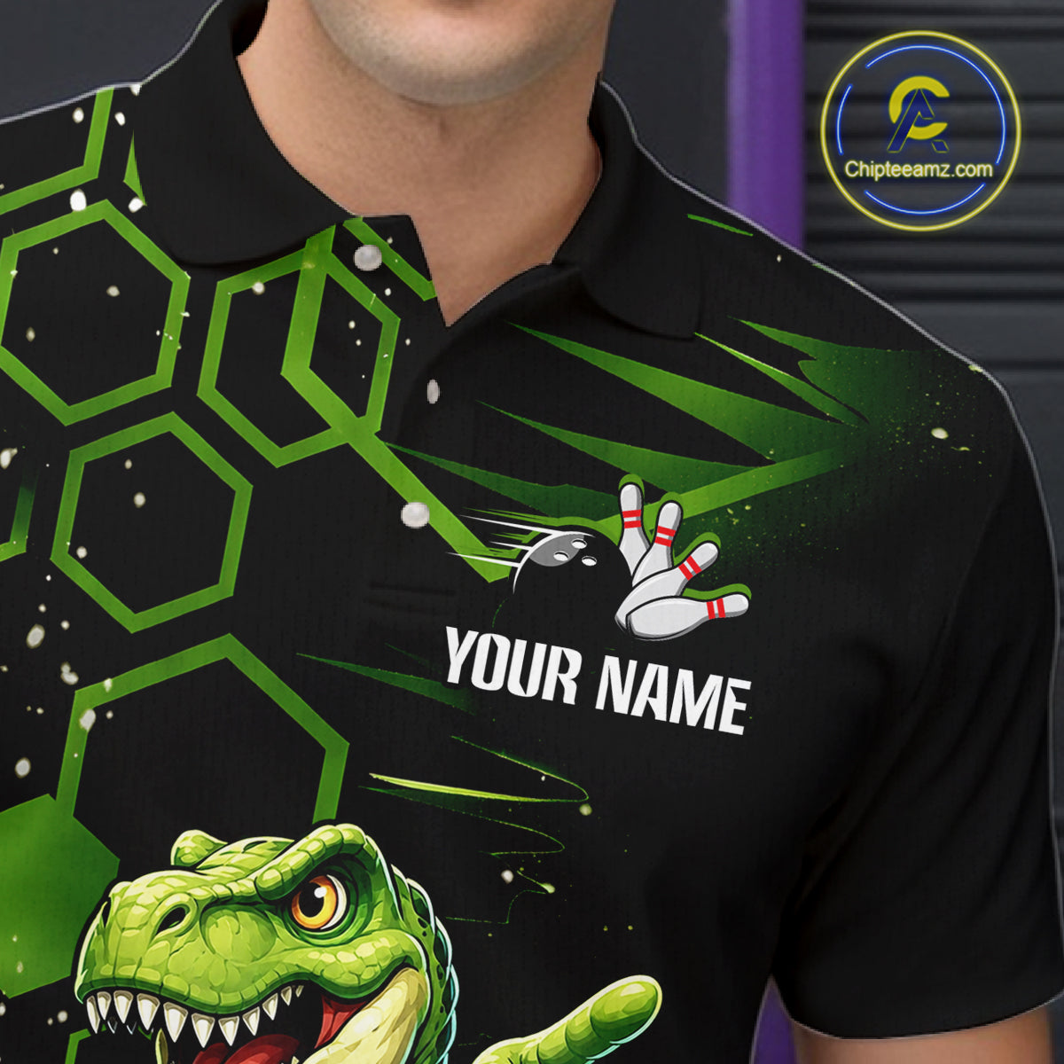 A close-up of a person wearing a black short-sleeve polo shirt with a green geometric pattern, a bowling pin graphic, and a green dinosaur graphic. The shirt has a placeholder text 'YOUR NAME' on the chest.