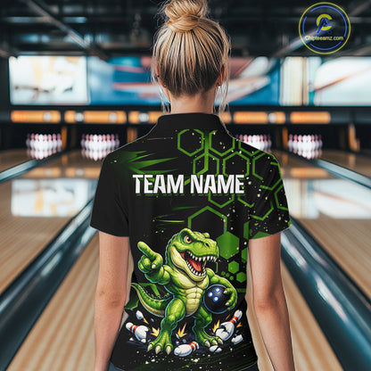 A woman viewed from behind wearing a black short-sleeve bowling shirt with a green cartoon dinosaur graphic and the text 'TEAM NAME' on the back, standing in a bowling alley.