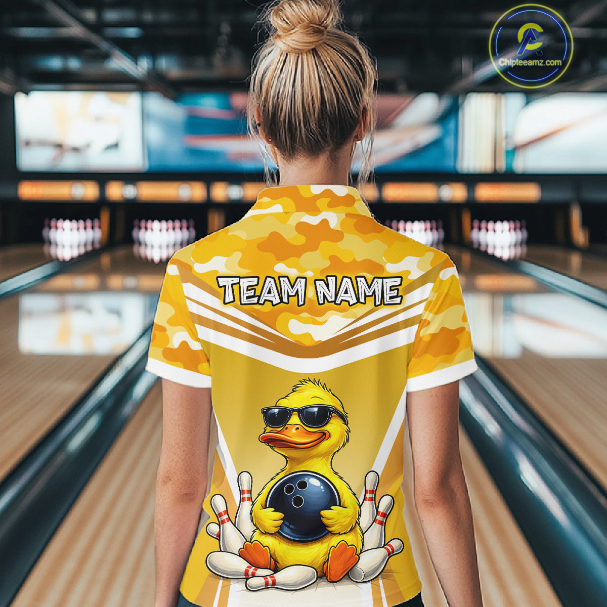 Female model wearing a custom yellow duck bowling polo shirt back view displaying the personalized team name above a cool cartoon duck wearing sunglasses graphic at the bowling alley