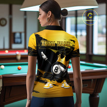 Load image into Gallery viewer, Back view of woman wearing custom black and gold geometric crown 8 ball billiard polo shirt in a billiard room showing personalized team name