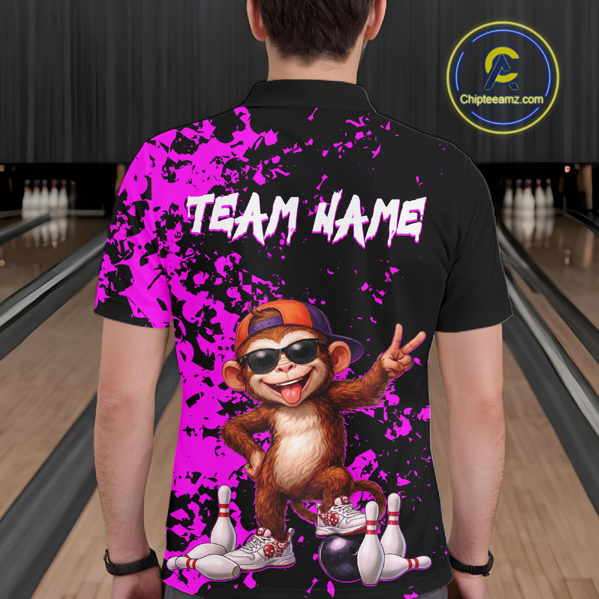 A person shown from the back wearing a black short-sleeve polo shirt with a bright purple paint-splatter design, white 'TEAM NAME' text, and a cartoon monkey graphic in an orange cap and sunglasses. Bowling alley lanes are visible in the background, and a circular 'Chipteamz'.