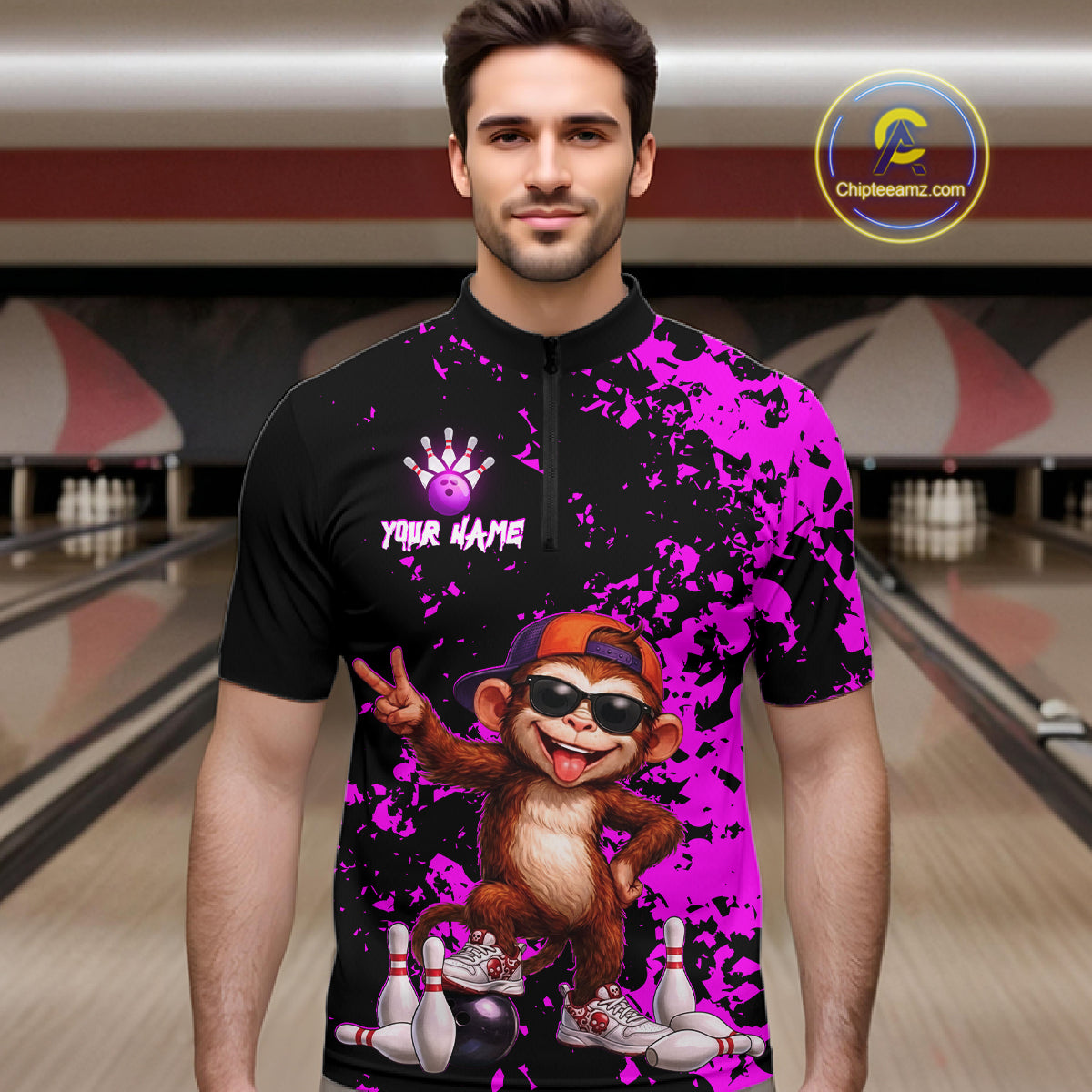 A man wearing a custom bowling-themed short-sleeve quarter-zip shirt with a black and bright purple splatter design, featuring a cartoon monkey graphic and the text 'YOUR NAME' on the chest. The background shows blurred bowling alley lanes.