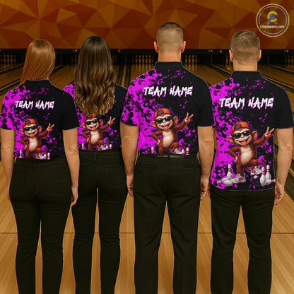 Four people standing in a bowling alley, viewed from behind, wearing matching black short-sleeve shirts with a bright purple paint-splatter design, a cartoon monkey graphic, and the text 'TEAM NAME' across the upper back. 