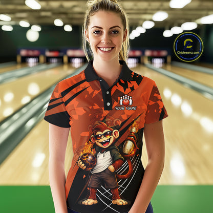 A woman wearing a custom orange and black bowling shirt with a cartoon monkey graphic, standing in a bowling alley. The shirt features a black collar, a custom logo with a paw print and the text 'YOUR NAME'