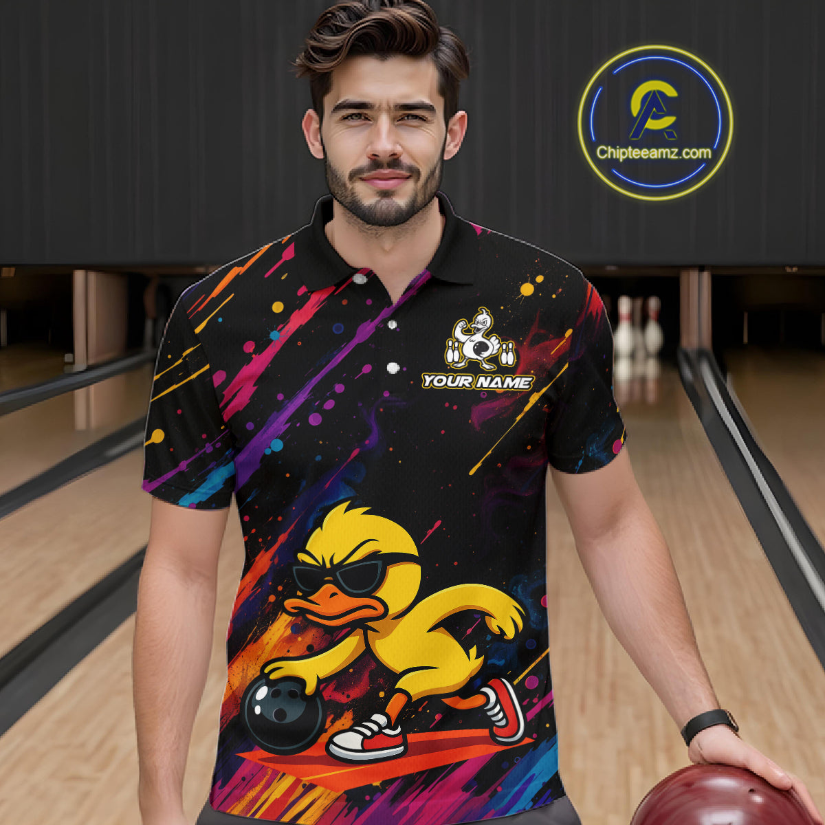 A man wearing a black short-sleeve bowling-themed polo shirt with a colorful paint splatter design and a cartoon duck graphic, standing in a bowling alley holding a bowling ball. A circular 'Chipleamz.