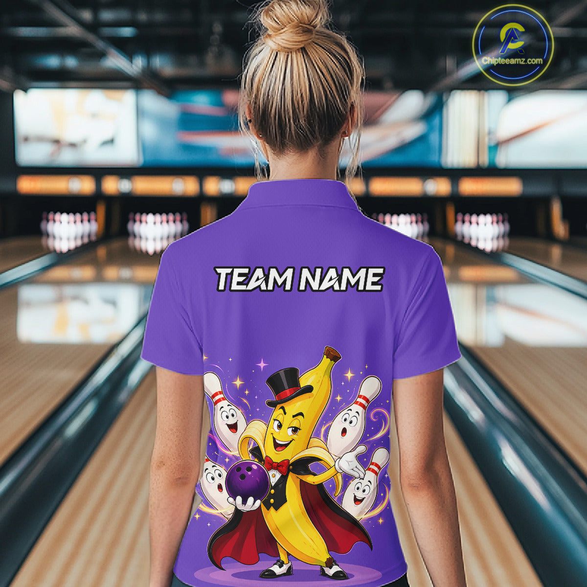Person wearing a purple bowling shirt with cartoon character design and 'TEAM NAME' text in a bowling alley.