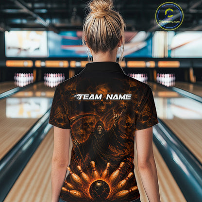 A woman viewed from behind wearing a black short-sleeve polo shirt with a fiery orange and brown grim reaper graphic and the text 'TEAM NAME' across the upper back, standing in a bowling alley.
