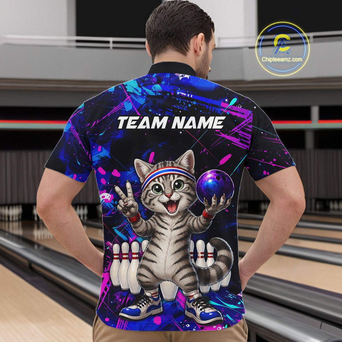 Person wearing a colorful bowling shirt with a cat graphic and 'TEAM NAME' text in a bowling alley.