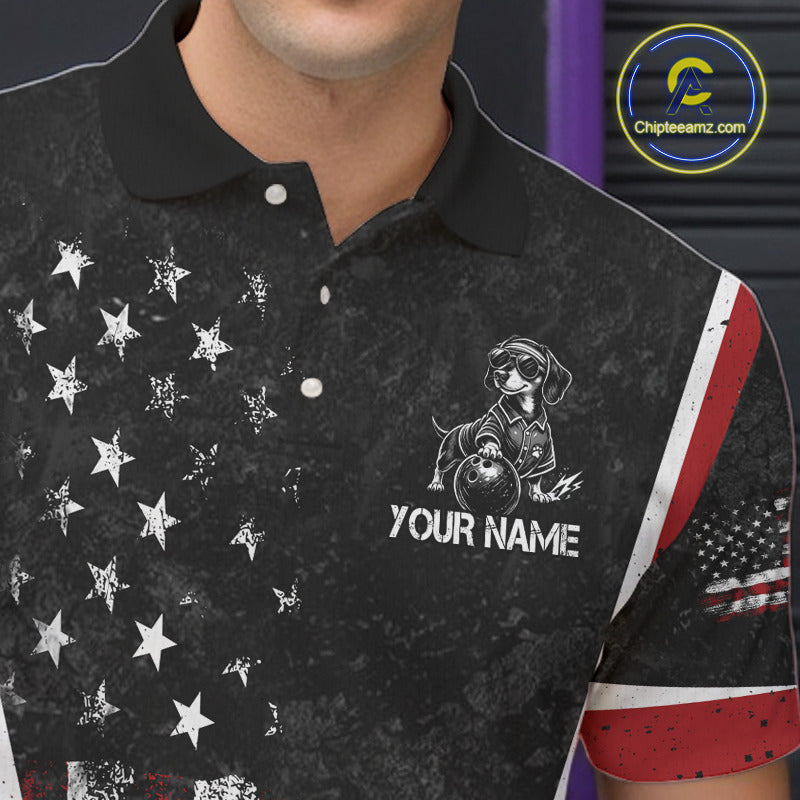 A close-up of a man wearing a black short-sleeve polo shirt with a distressed American flag theme. The shirt features white stars on the left side, a white graphic of a dachshund wearing sunglasses and a motorcycle helmet on the right chest, and the customizable text 'YOUR NAME' below it.