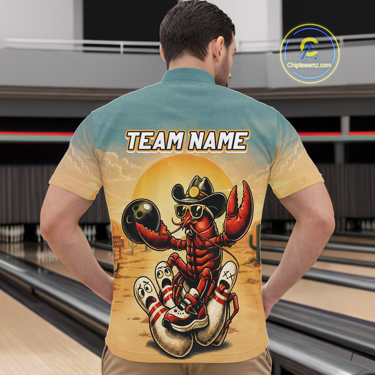 Man wearing a shirt with a colorful design of a crawfish in a cowboy hat and boots, standing in back of a bowling alley.