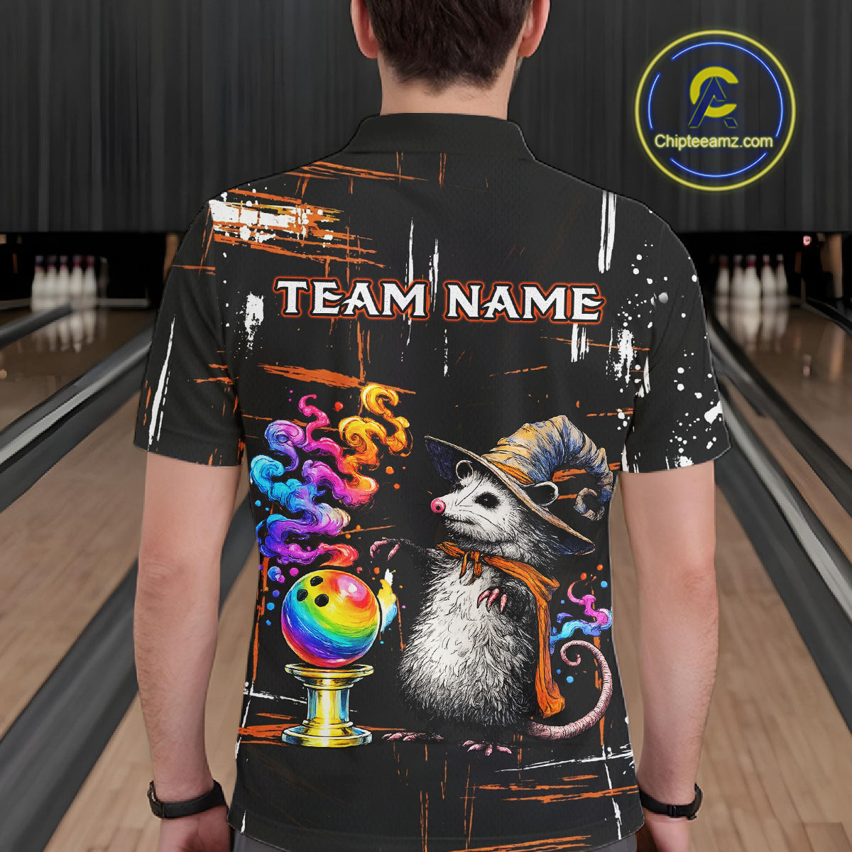 A person viewed from behind wearing a black short-sleeve bowling shirt with a large colorful graphic of a opossum wearing a wizard hat and scarf, a rainbow bowling ball, smoke, and the text 'TEAM NAME' across the back. The background shows bowling lanes.