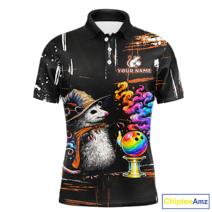 A black short-sleeve polo shirt with a colorful graphic print of a opossum in a witch hat next to a rainbow bowling ball, on a white background.