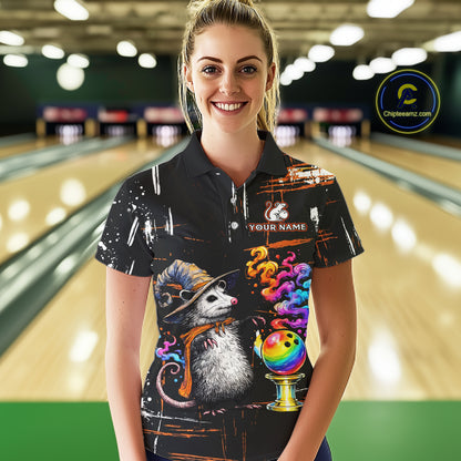 A woman stands in a bowling alley wearing a black short-sleeve polo shirt with a colorful graphic print featuring a hedgehog, bowling balls, bowling pins, and the text 'YOUR NAME' 