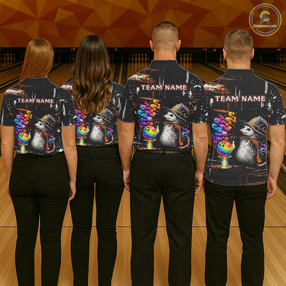 Four people standing with their backs to the camera in a bowling alley, wearing matching dark short-sleeve shirts with a colorful graphic print of opossum wearing hats and rainbow bowls, plus 'TEAM NAME' text on the back.