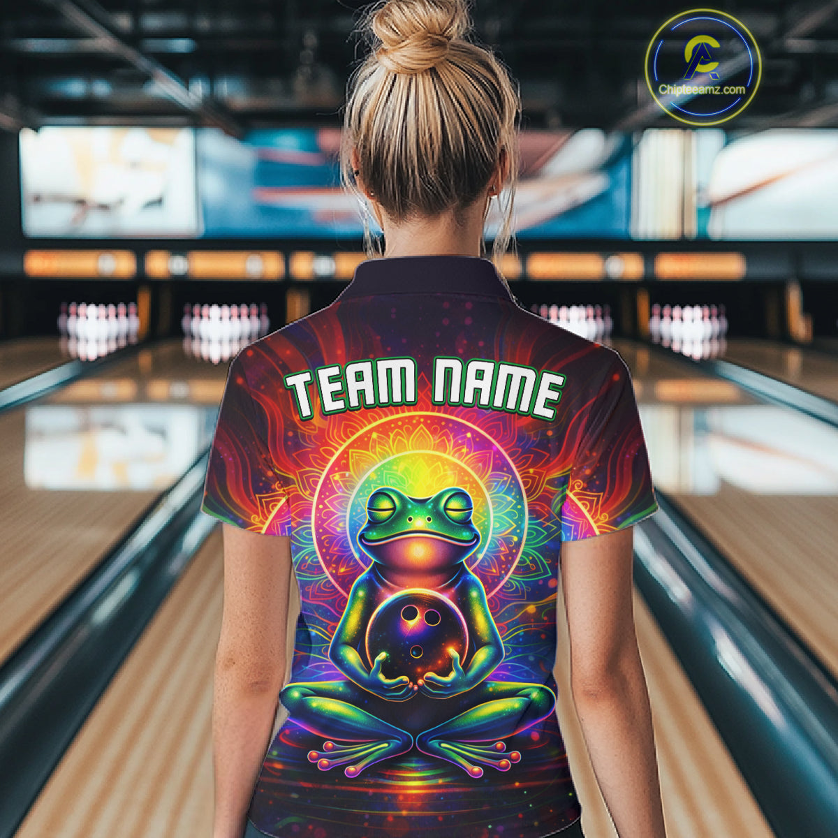 Female model wearing a custom zen frog bowling quarter-zip shirt back view displaying the personalized team name above a vibrant neon frog artwork at the bowling alley