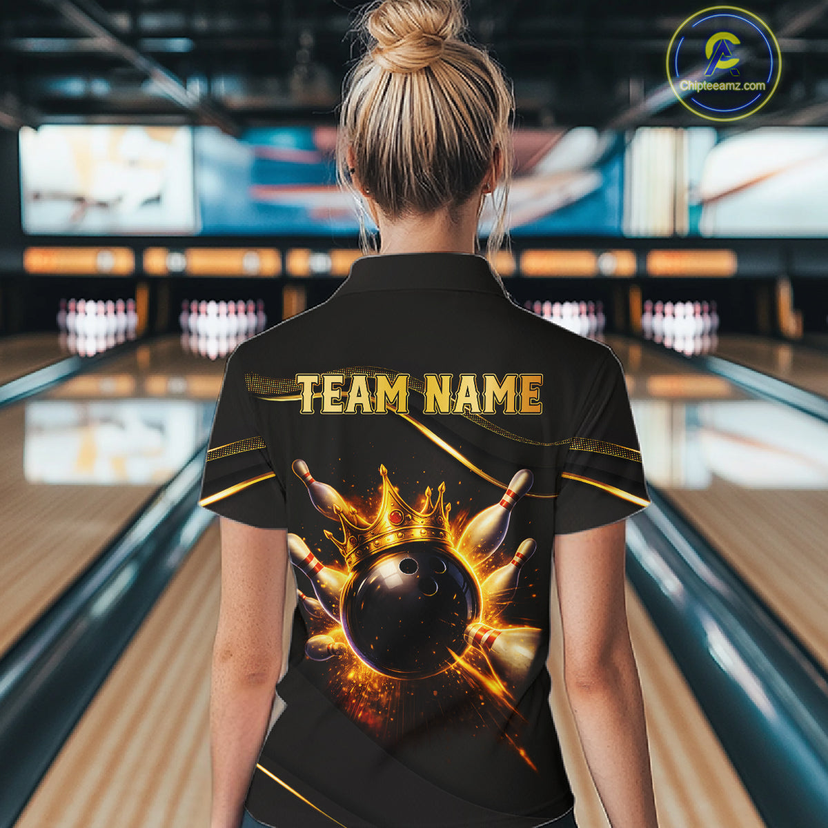 A woman viewed from behind wearing a black bowling-themed shirt with a large graphic of a bowling ball and pins and the text 'TEAM NAME' on the back, standing in a bowling alley.