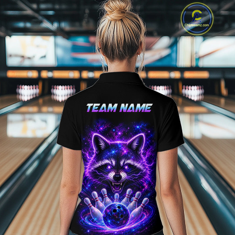 A woman viewed from behind wearing a black short-sleeve polo shirt with a large colorful raccoon graphic and the text 'TEAM NAME' on the back, standing in a bowling alley.