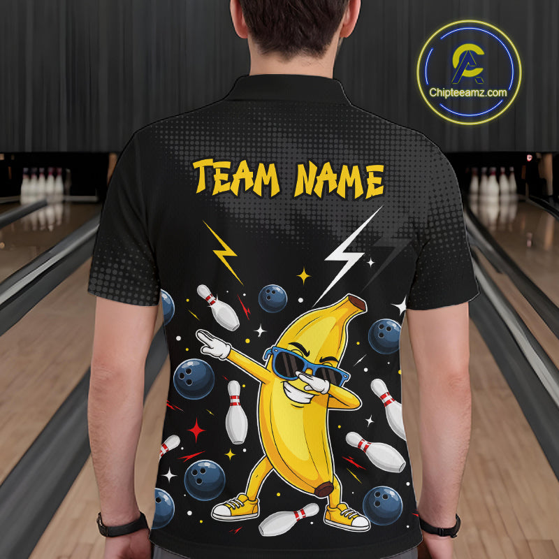 Man wearing a black polo with a colorful design of a banana character and bowling elements, standing in a bowling alley.