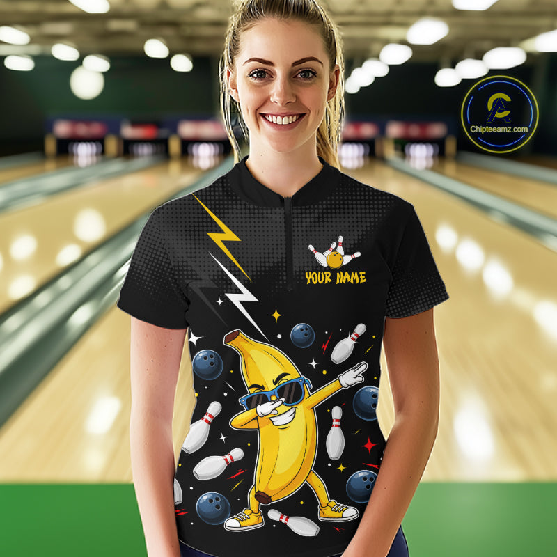 Person wearing a black bowling-themed shirt with a banana character in a bowling alley.