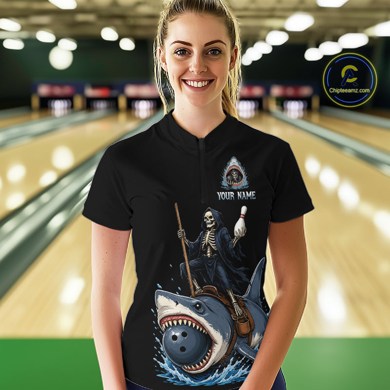 A woman stands in a bowling alley wearing a black short-sleeve polo shirt with a large graphic print of a grim reaper riding a shark. The shirt has a customizable design with a small eye logo and the text 'YOUR NAME'.