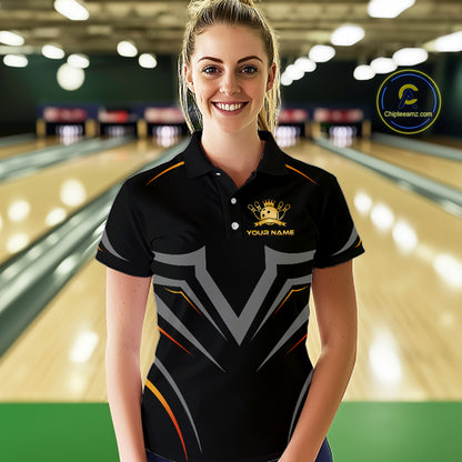 Woman wearing a black bowling shirt with a logo and text in a bowling alley.