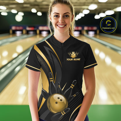 Woman wearing a black and gold bowling shirt with a logo and text in a bowling alley.