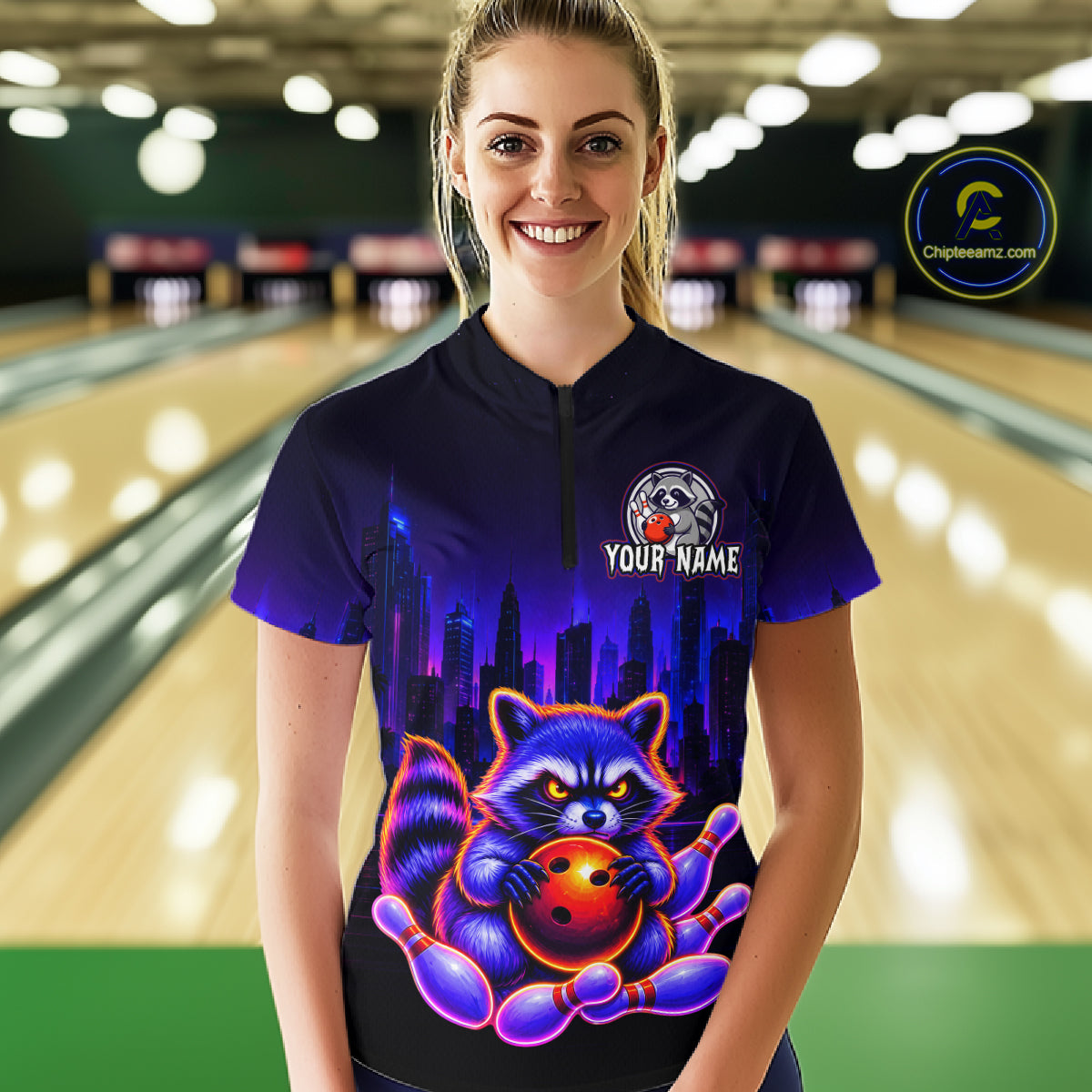 Women wearing bowling quarter zip shirt featuring a raccoon holding a bowling ball framed by pins with purple city skyline background.