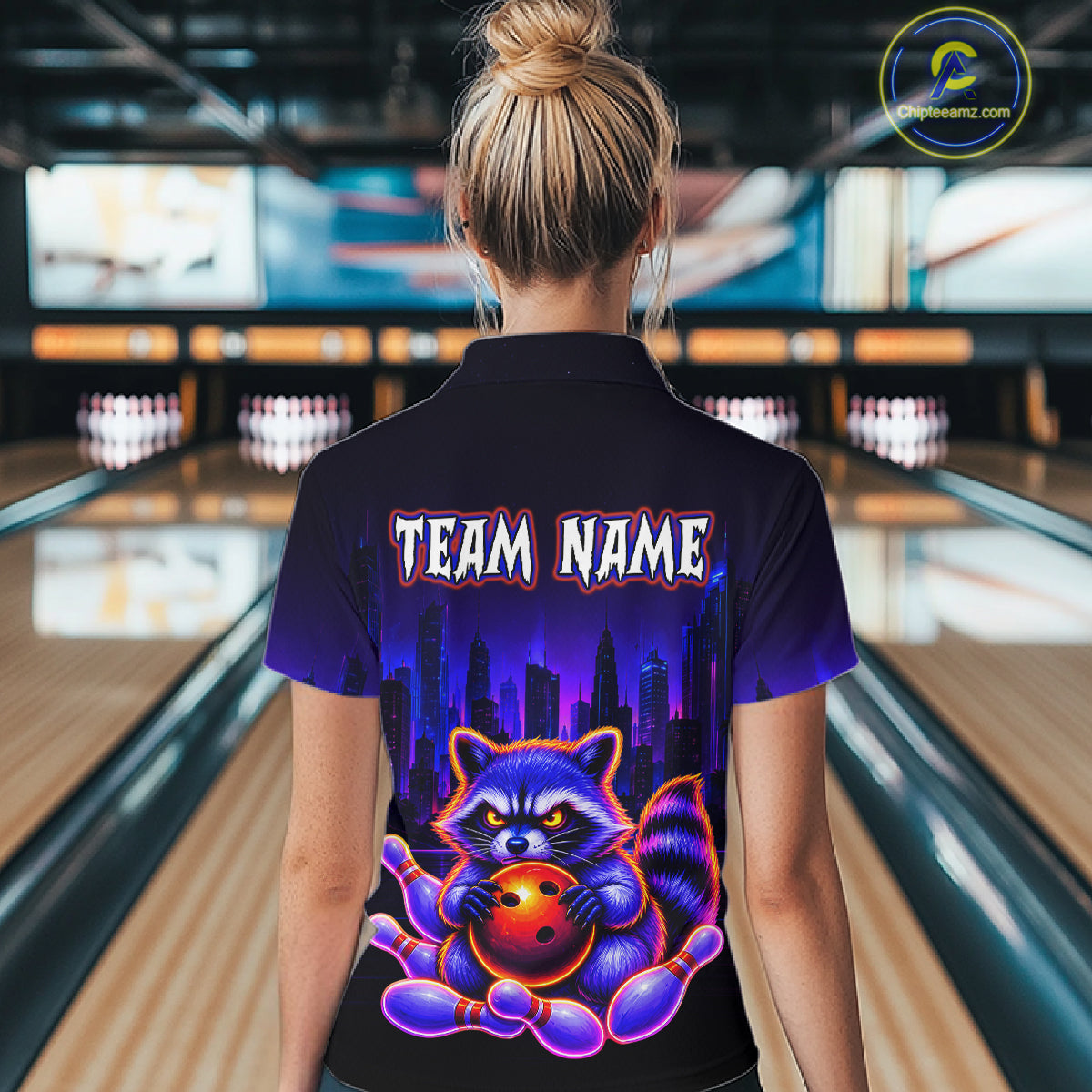 Women wearing bowling polo shirt featuring a raccoon holding a bowling ball framed by pins with purple city skyline background.