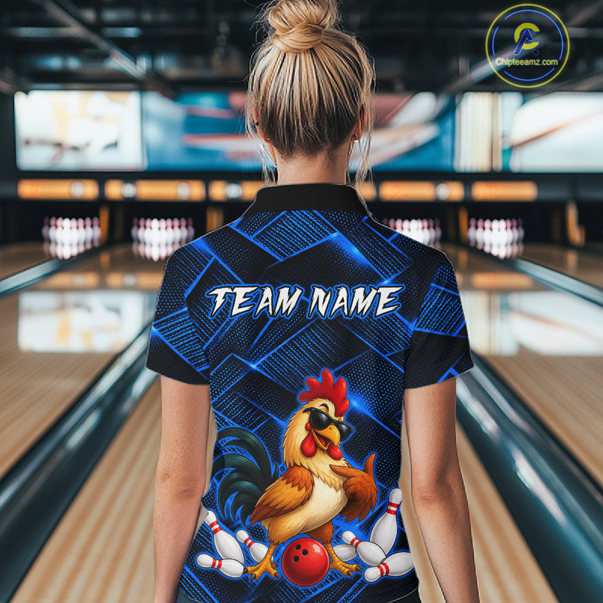 Woman wearing a blue and black bowling quarter zip shirt featuring a cool rooster mascot wearing sunglasses, a red bowling ball, bowling pins, and custom team name text.