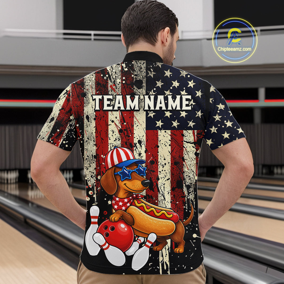 Man wearing a shirt with a dachshund hot dog graphic and 'TEAM NAME' text in a bowling alley.