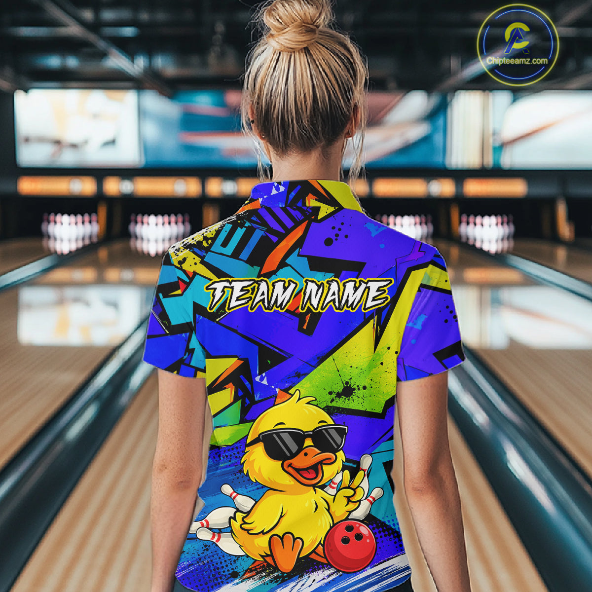 Person wearing a colorful bowling shirt with a duck graphic in a bowling alley.
