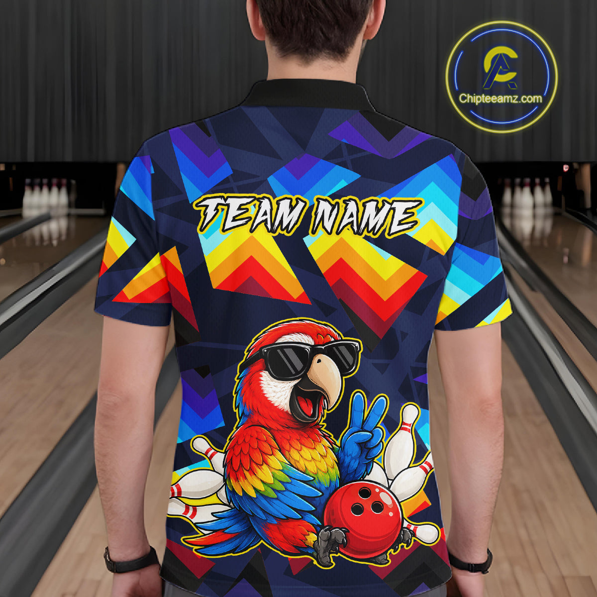 A person viewed from behind wearing a short-sleeve bowling-themed graphic shirt in a bowling alley. The shirt features a colorful parrot, bowling pins, a bowling ball, and the text 'TEAM NAME' on the back.