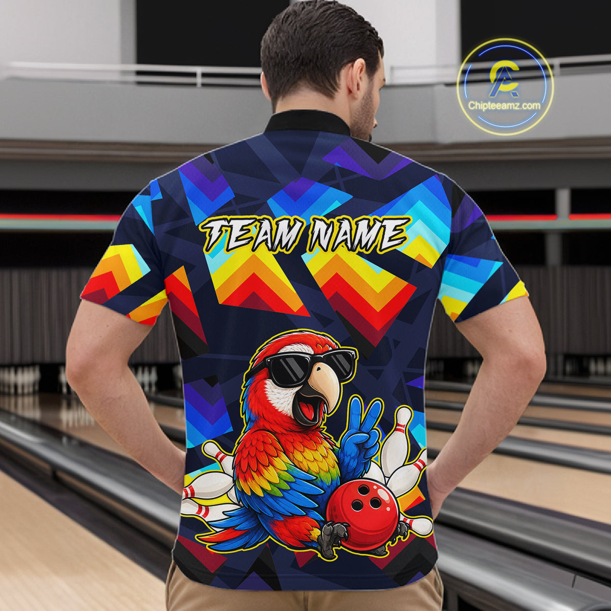 A man viewed from behind wearing a short-sleeve bowling-themed polo shirt with a colorful geometric pattern and a large parrot graphic on the back. The shirt features the text 'TEAM NAME' and a red bowling ball with white bowling pins near the lower back.
