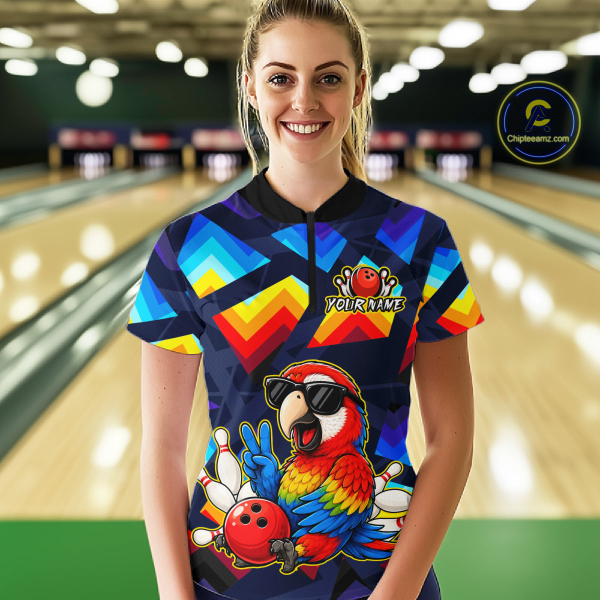 A woman stands in a bowling alley wearing a short-sleeve custom bowling shirt with a colorful geometric pattern and a large parrot graphic on the front. The shirt features a black collar and a black-and-white logo on the left chest that reads 'YOURNAME'.