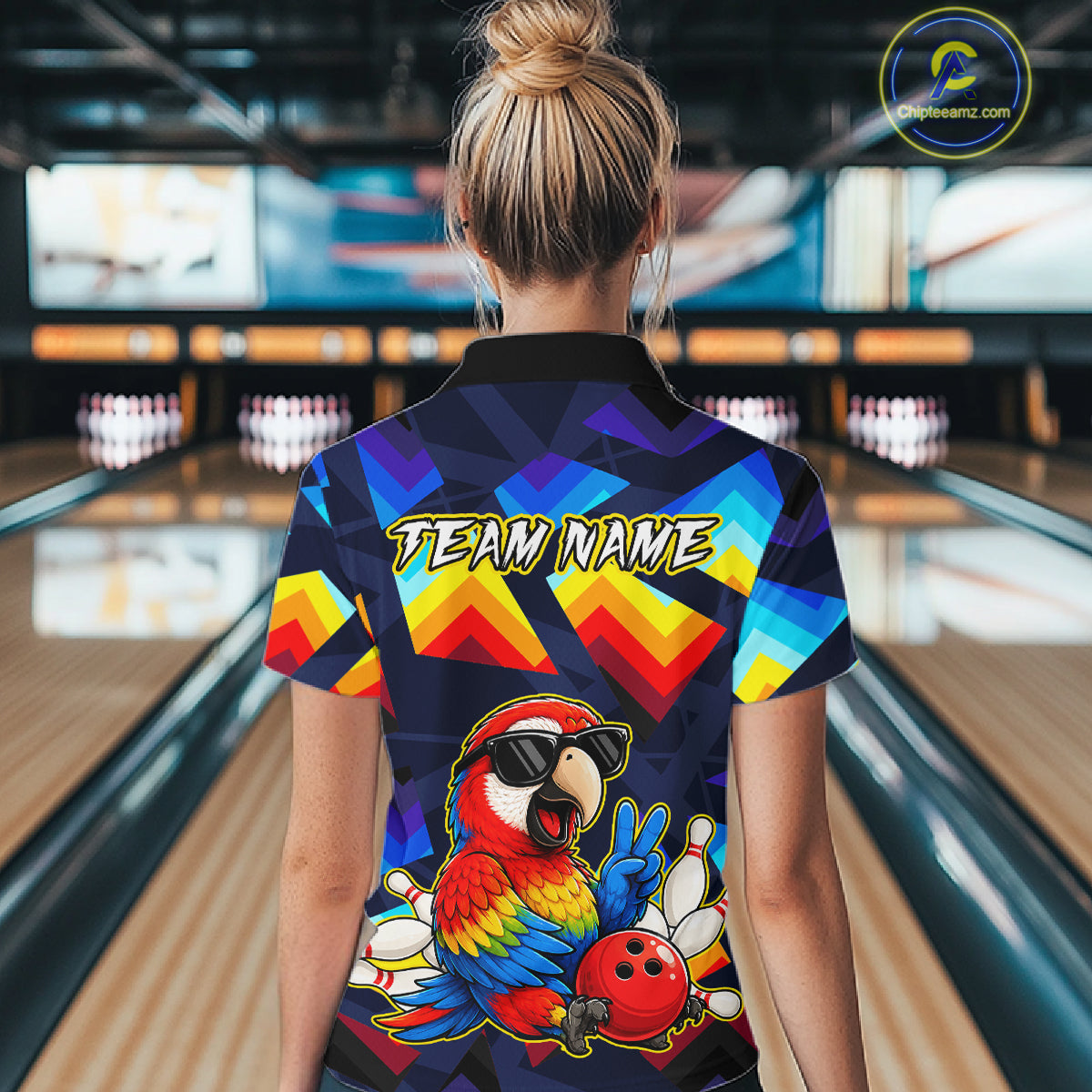 A woman viewed from behind wearing a short-sleeve bowling-themed polo shirt with a colorful geometric pattern and a large parrot graphic on the back, standing in a bowling alley.